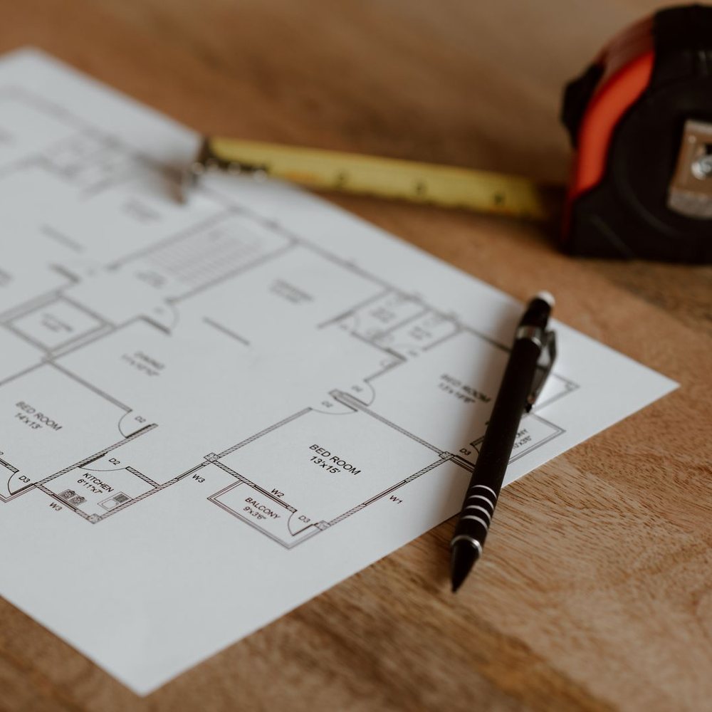 A floor plan on a wooden desk with a pen and tape measure, ready to be discussed